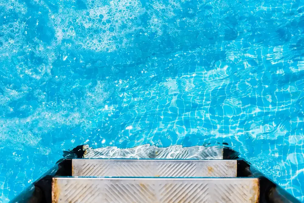 Sunlit, crystal-clear pool water beside the pool steps